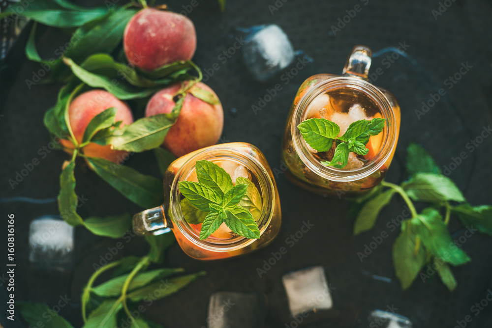 Summer refreshing cold peach ice tea with fresh mint in glass jars on metal tray background, top vie