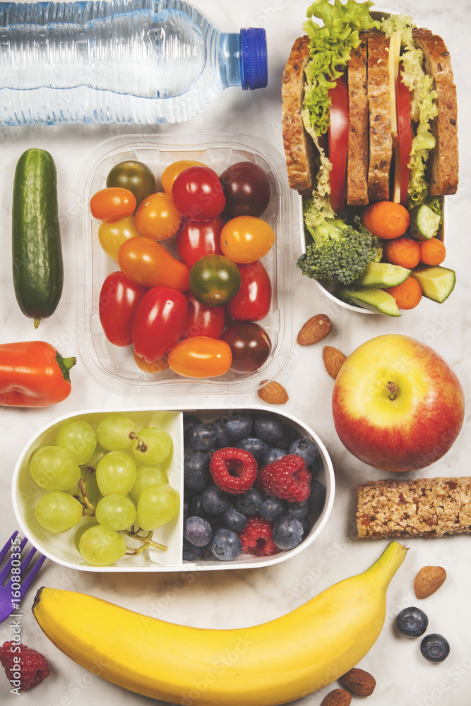 Healthy lunch box with sandwich and fresh vegetables, bottle of water and fruits