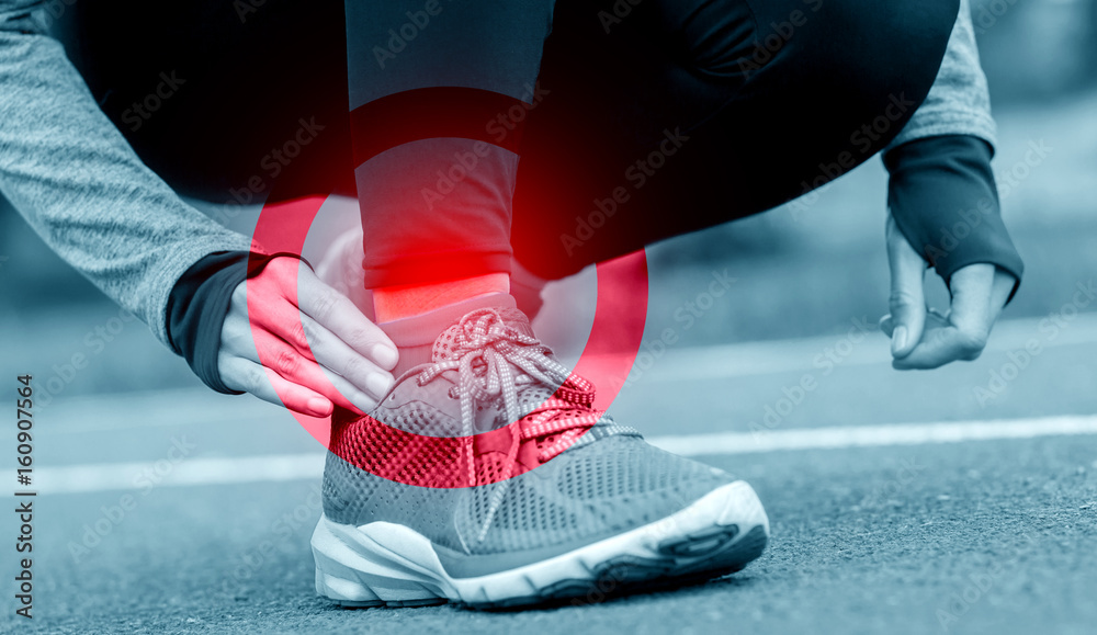 Athletic woman on running track touching hurt leg with ankle injury