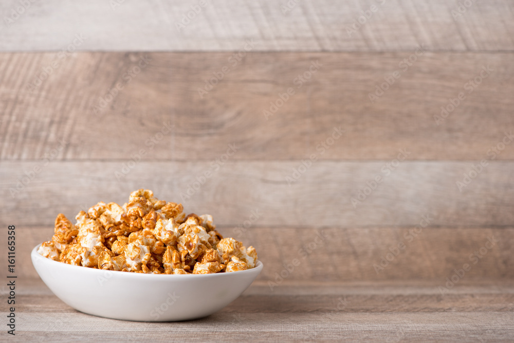 Caramel opcorn in bowl on the wooden table.