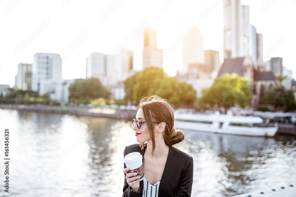 年轻的女商人坐在法兰克福市的桥上，在户外喝咖啡休息