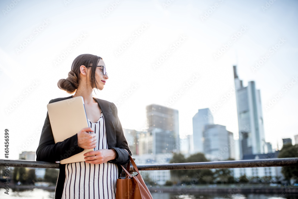 Young businesswoman having a coffee break outdoors sitting on the bridge in Frankfurt city during th