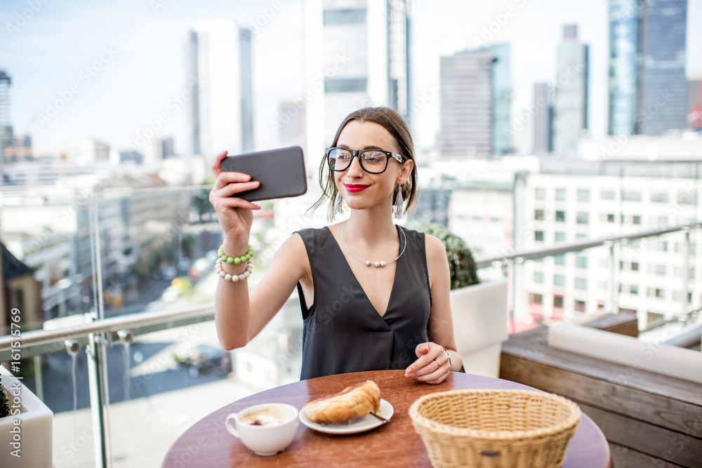 Happy businesswoman making selfie portrait sitting on the terrace during the breakfast with skyscrap