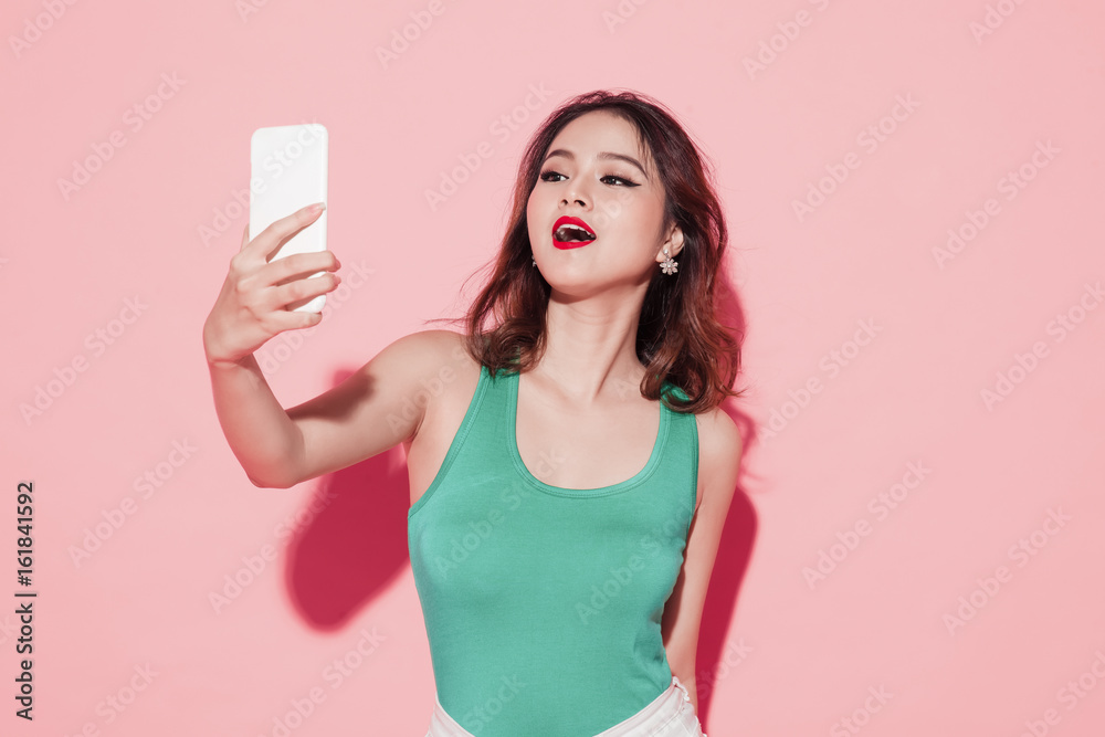 Asian young woman taking selfie photo on pink background.