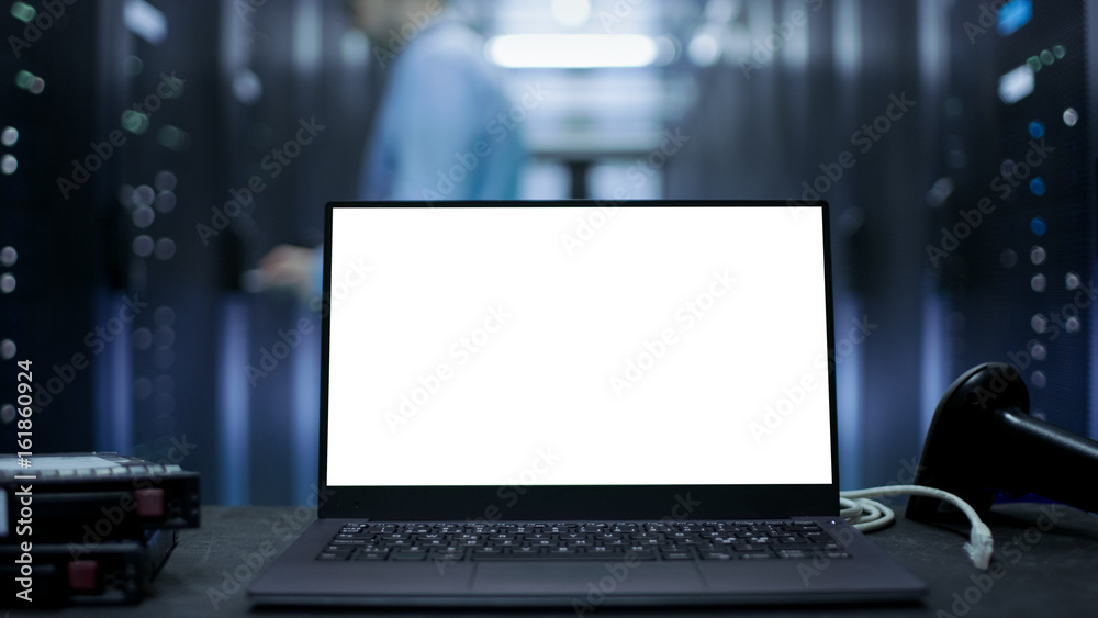 Laptop with White Screen on It Stands on The Table. In the Background Data Center With Rows of Serve