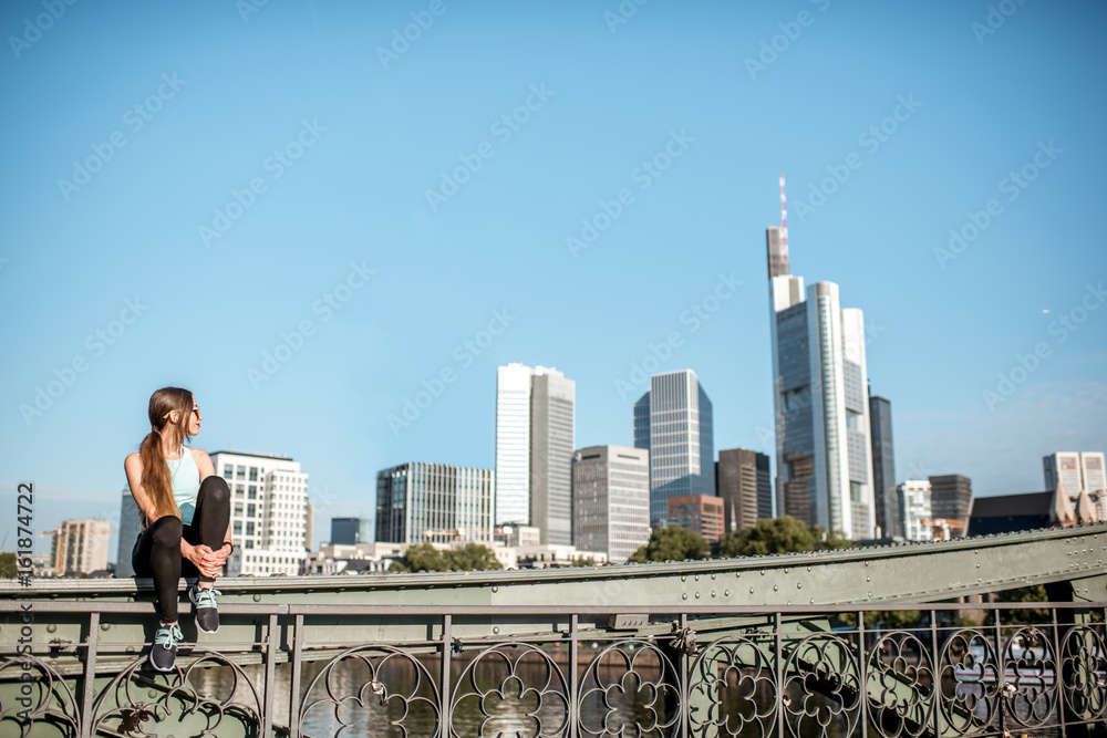 Young woman in sportswear sitting on the bridge after the training with great view on the modern cit