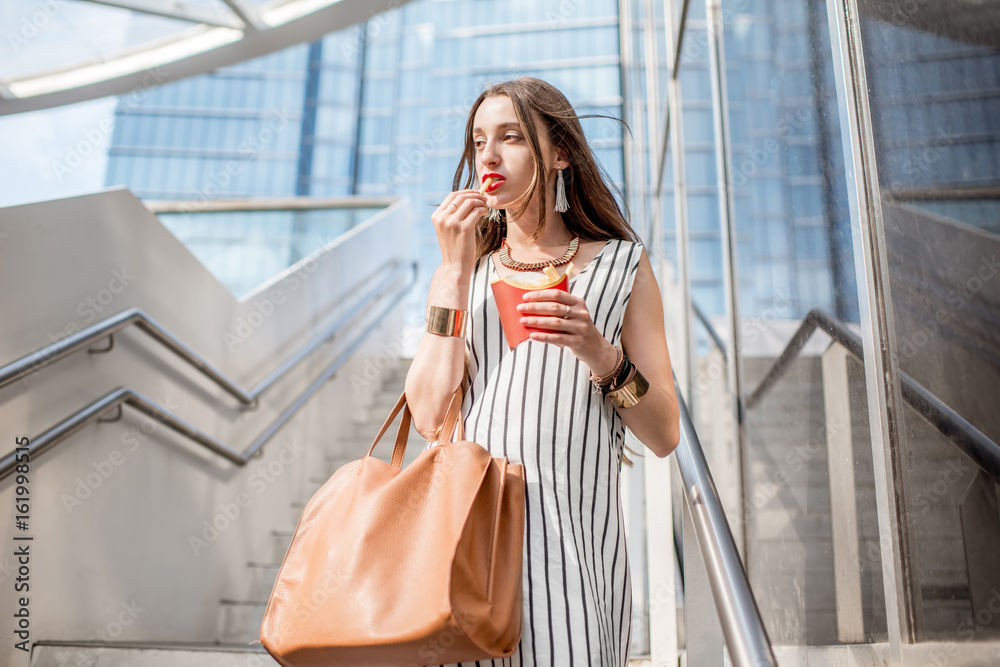 一位年轻的女商人在户外现代餐厅附近的楼梯上用frech薯条吃快餐