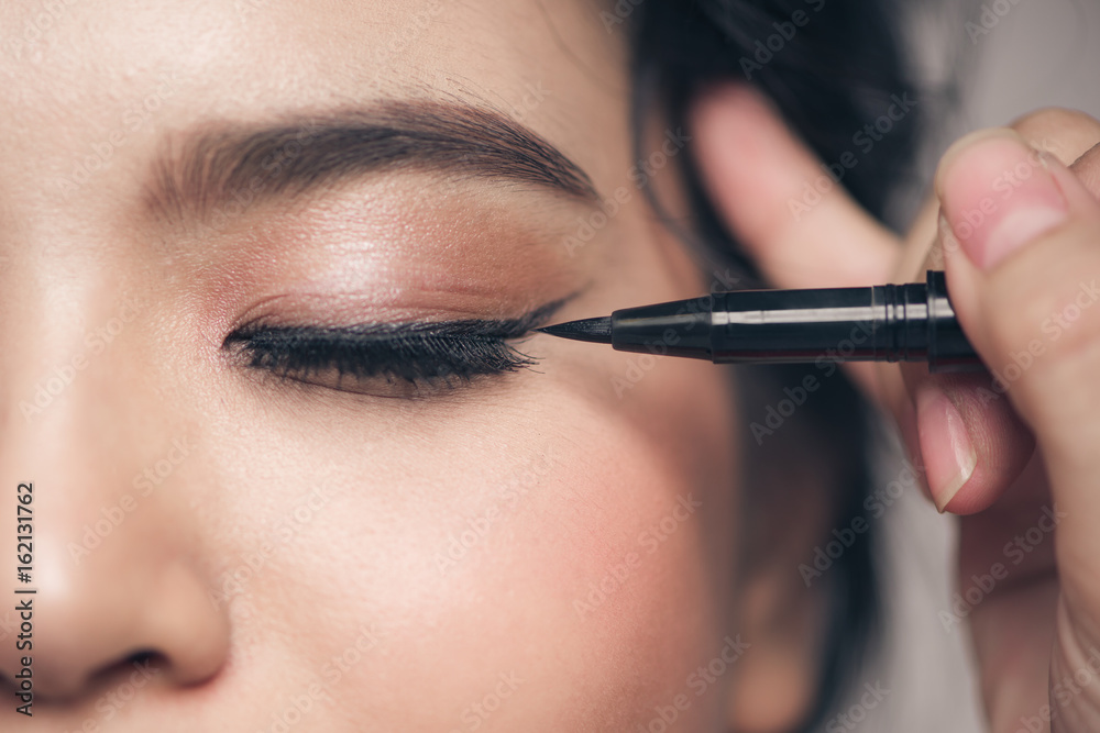 Close-up portrait of beautiful girl touching black mascara to her lashes