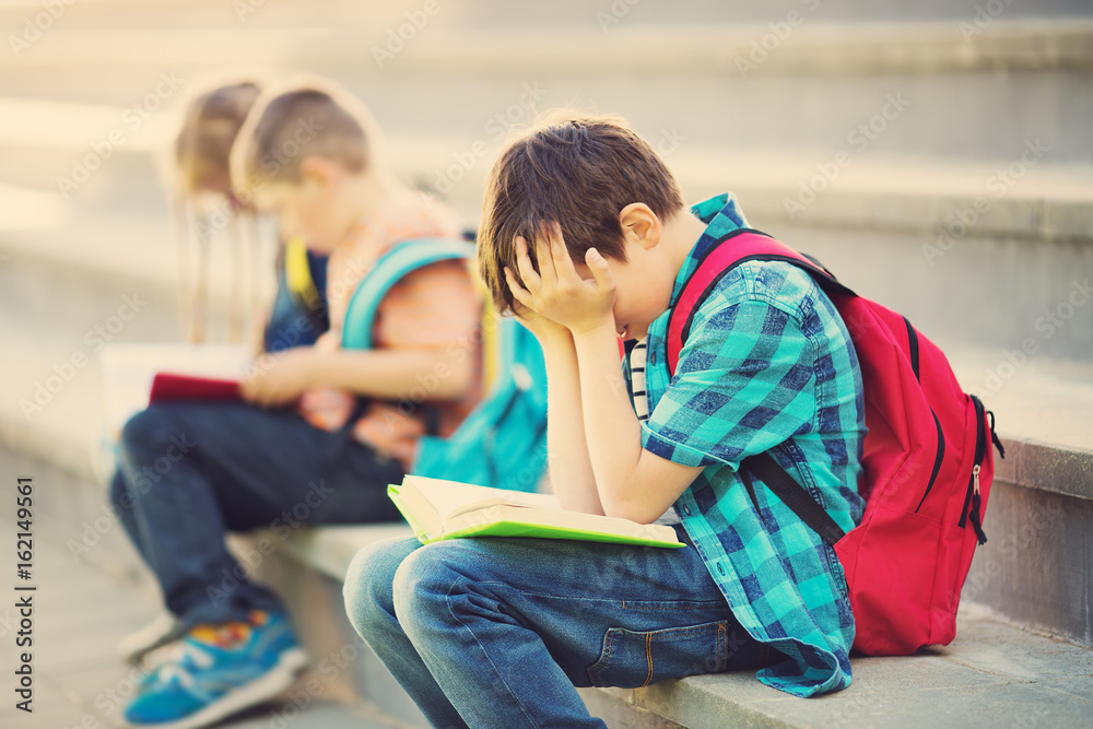 Children with rucksacks sitting on the stairs near school. Pupils with books and backpacks outdoors