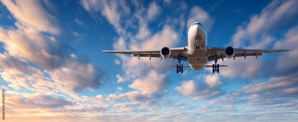 Landing airplane. Landscape with white passenger airplane is flying in the blue sky with clouds at c