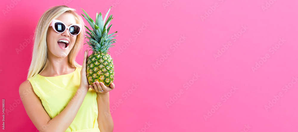 Happy young woman holding a pineapple on a pink background