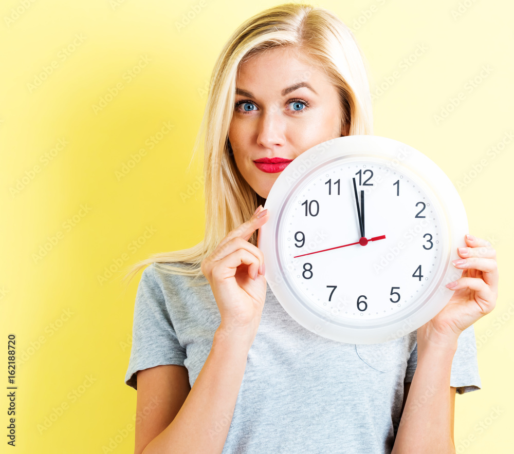 Young woman holding a clock showing nearly 12 