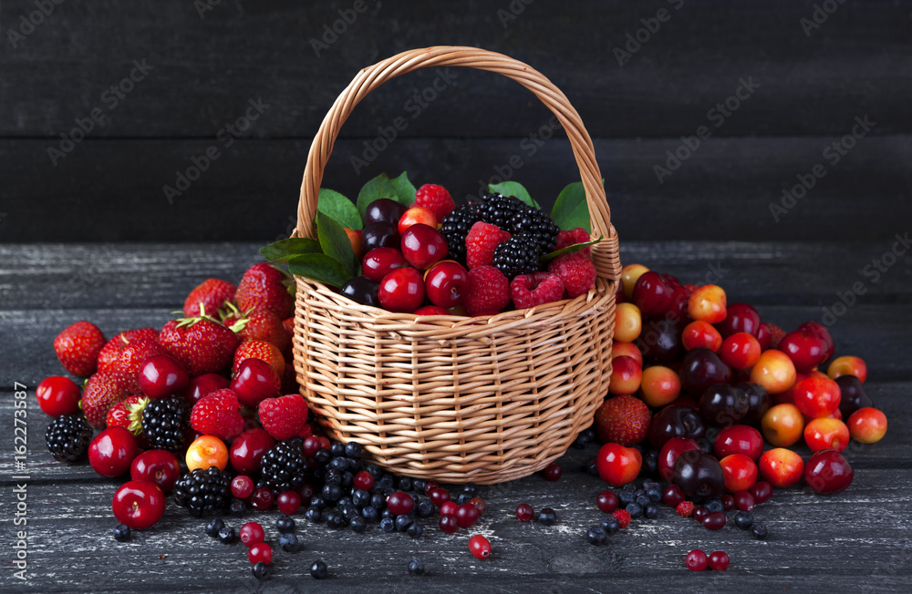 Fresh forest berries in basket on rustic wooden background. Copy space