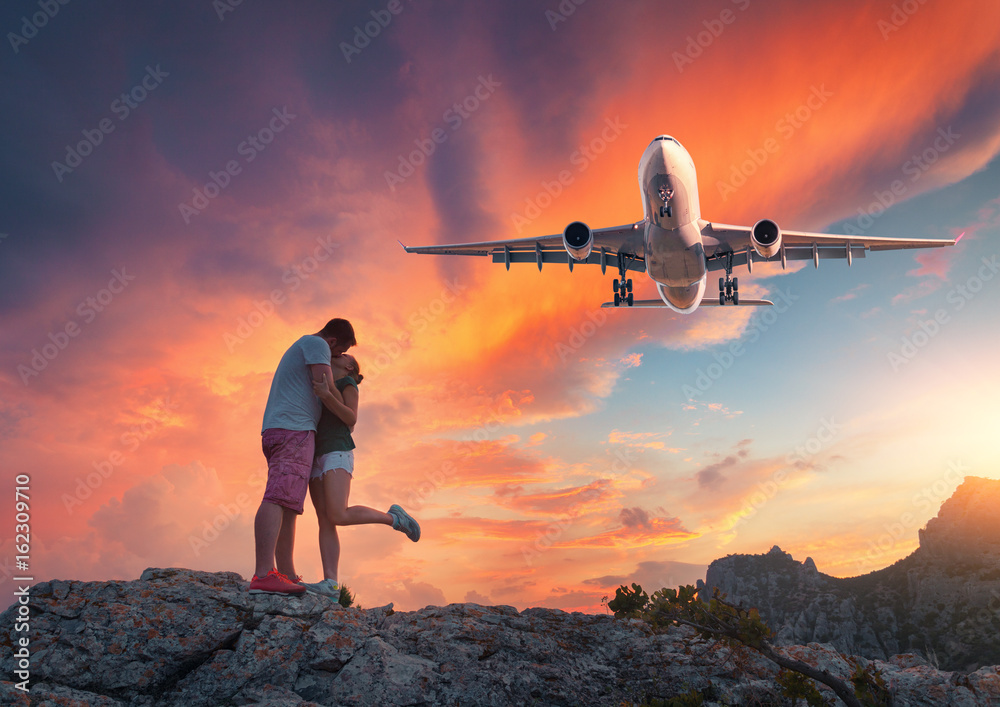 Airplane and hugging and kissing man and woman on the mountain peak at sunset. Landscape with landin