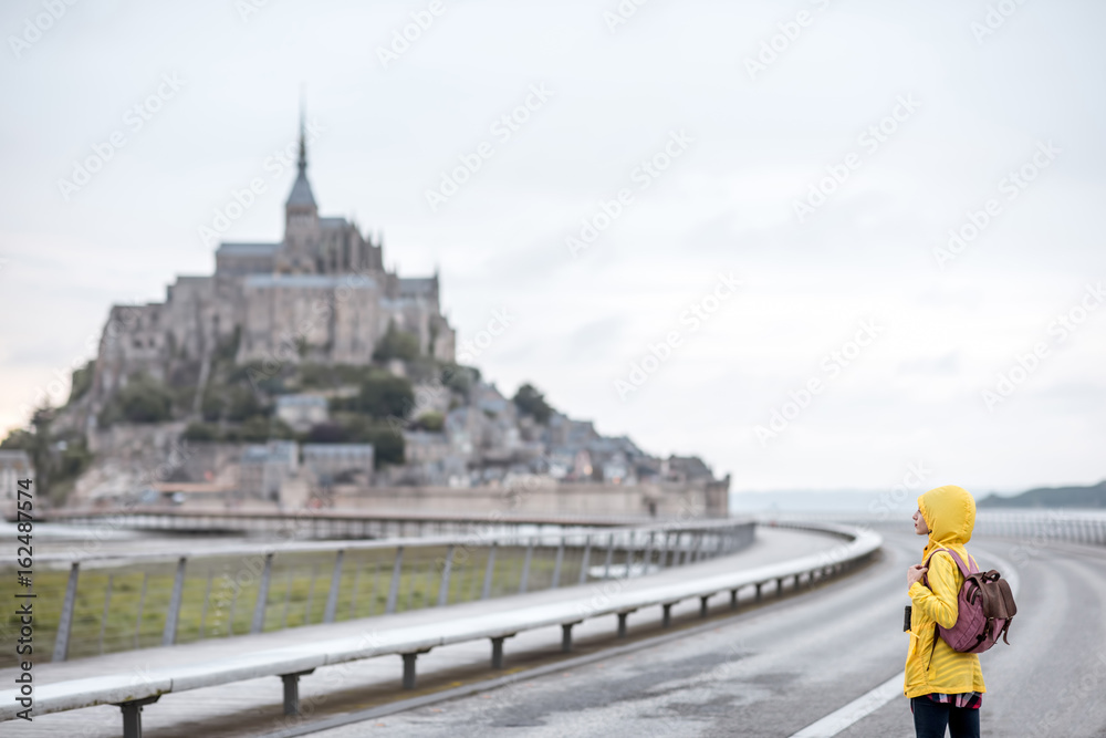 Young female traveler in yellow raincoat on the road to famous saint Michel island in France