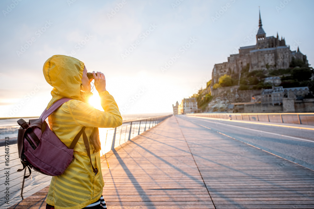 Young female traveler in yellow raincoat on the road to famous saint Michel island in France