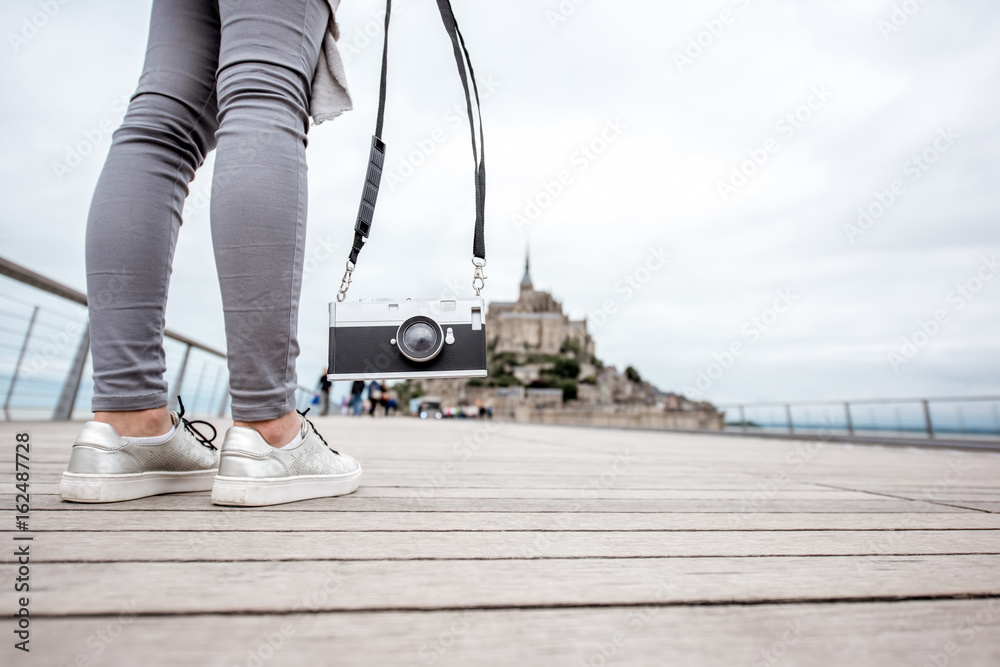 Woman holding photo camera stnading on the road to famous saint Michel island in France