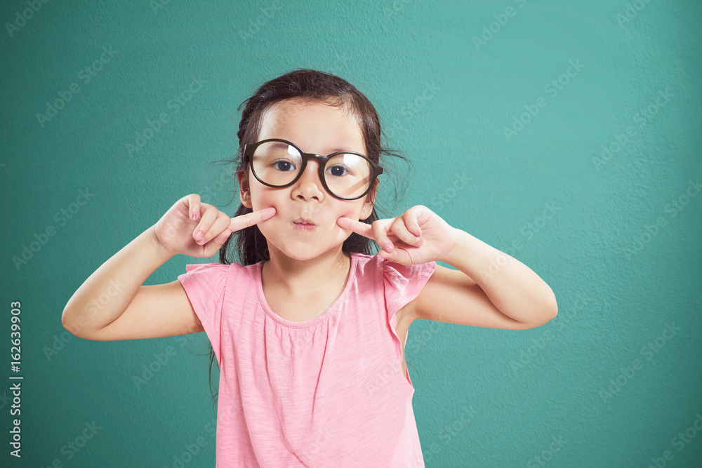 Happy little Asian girl with glasses smiling isolated on vintage mint green background .