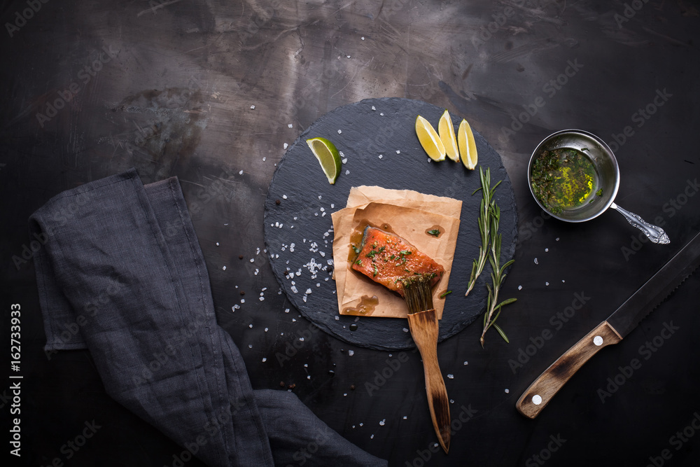 A piece of raw salmon oiled marinade with spices, lemon, spices and olive oil with brush on slate st