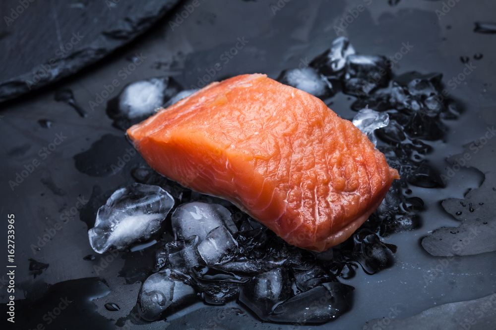 A piece of raw fish on ice on a dark metallic background. Close-up. Fish meal. Salmon steak.