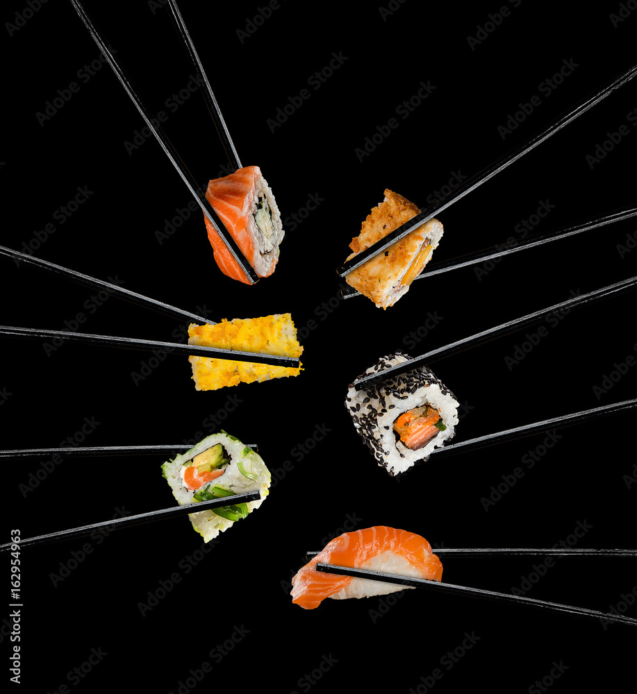 Sushi pieces placed between chopsticks, on black background