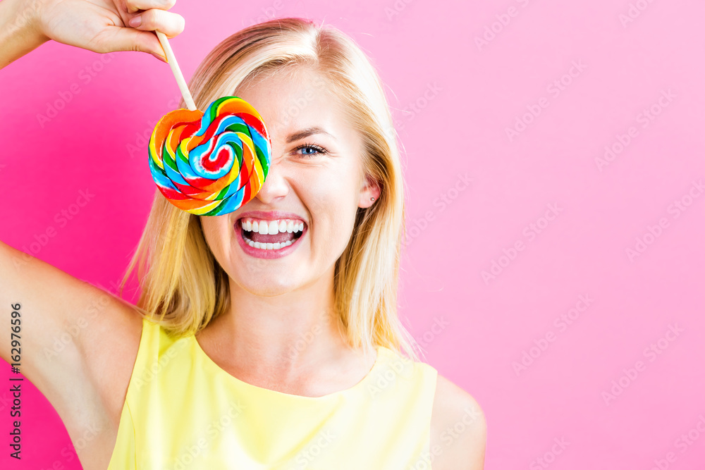 Young woman eating a lollipop on a pink background