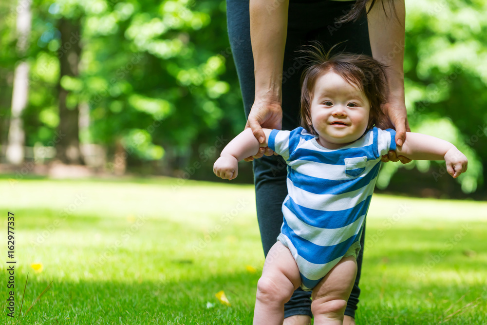 Baby boy learning to walk outside with the help of his parents