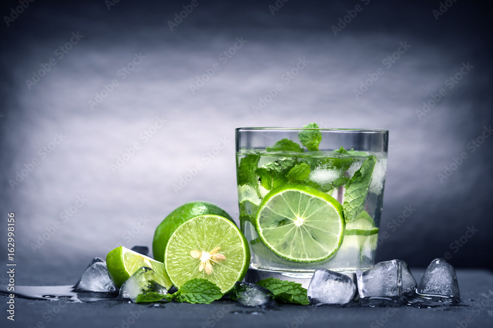 Close up fresh mojito cocktail with fresh lime and mint leaf on black stone background