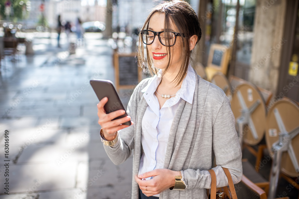 Young and stylish businesswoman standing with phone on the street with cafes in Lyon old town