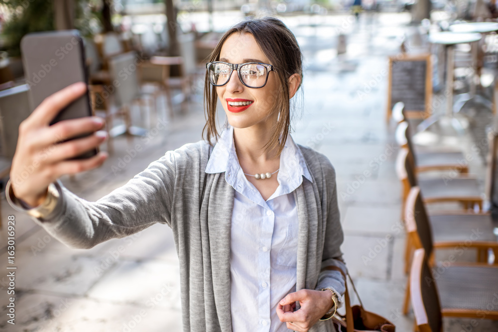 Young and stylish businesswoman standing with phone on the street with cafes in Lyon old town