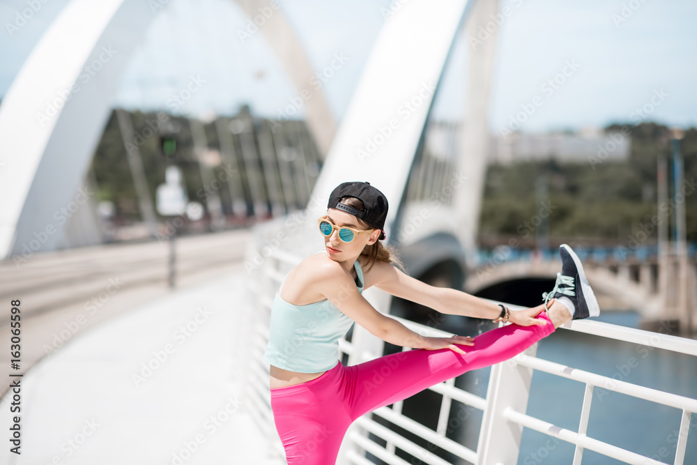 Young woman in bright sportswear exercising outdoors on the white modern bridge in Lyon city