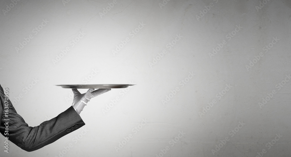 Hand of butler holding empty metal tray against concrete background