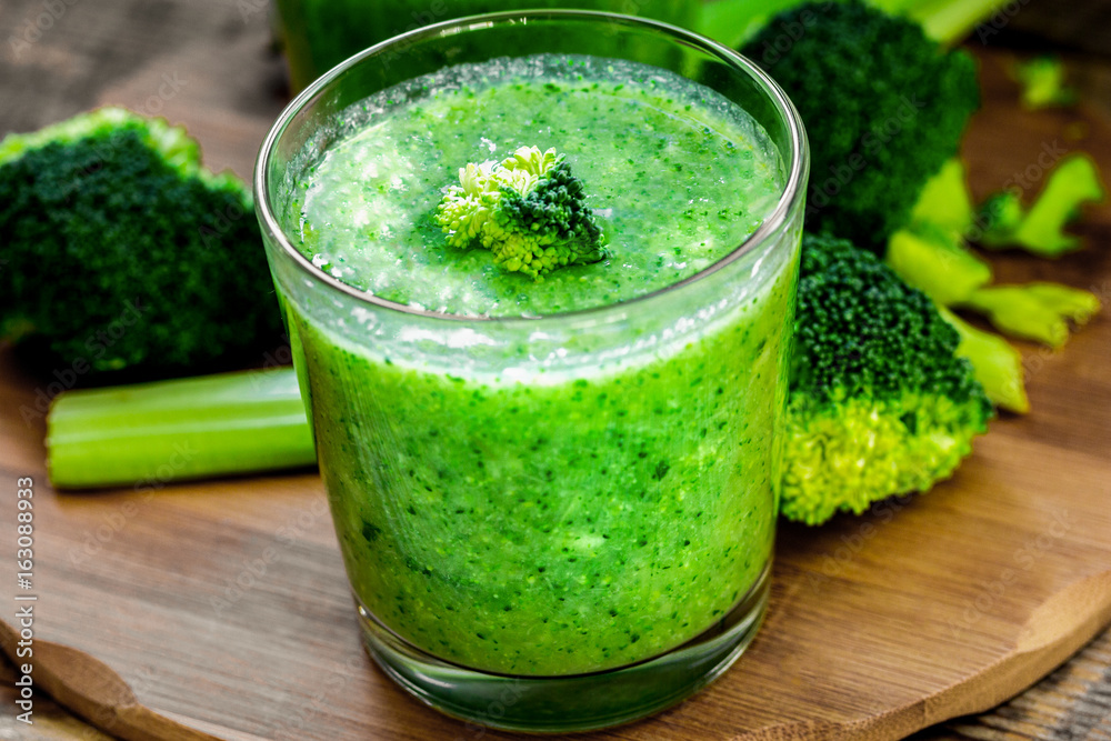 Green vegetable smoothie in glass at wooden background