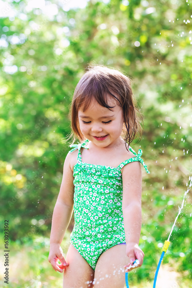 Happy toddler girl playing with sprinkler outside