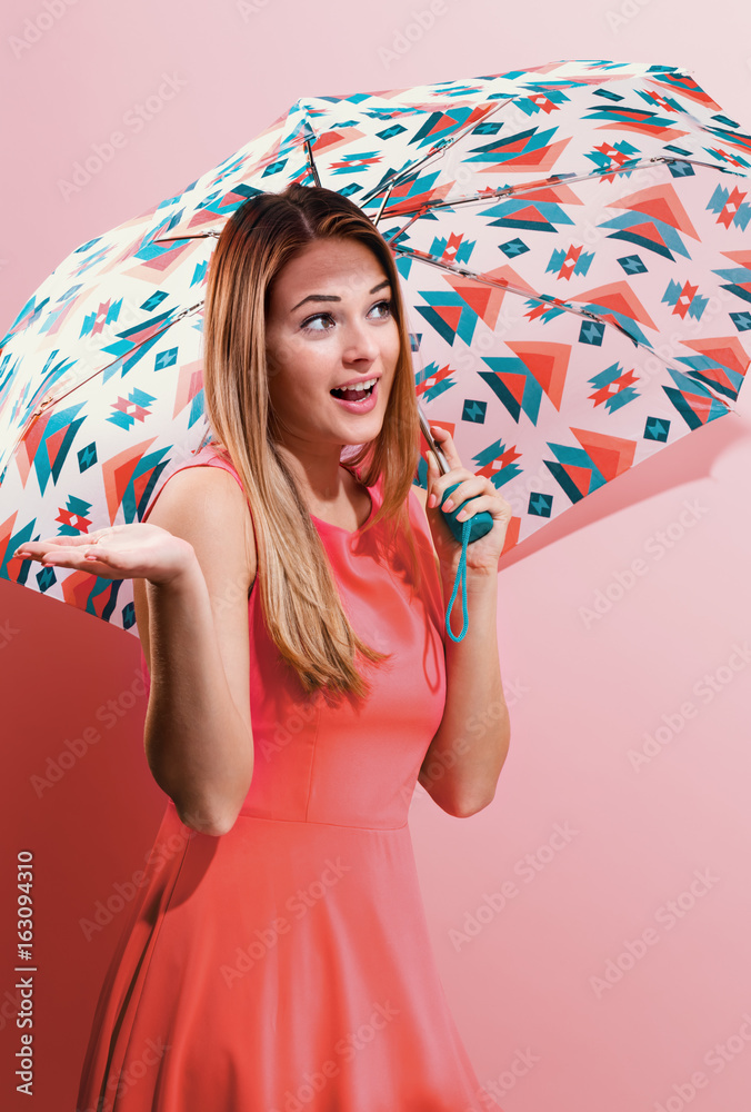 Happy young woman holding an umbrella on a pink background