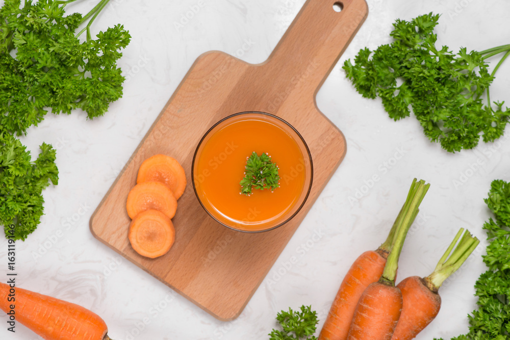 Glass of fresh carrot juice with vegetables on table.