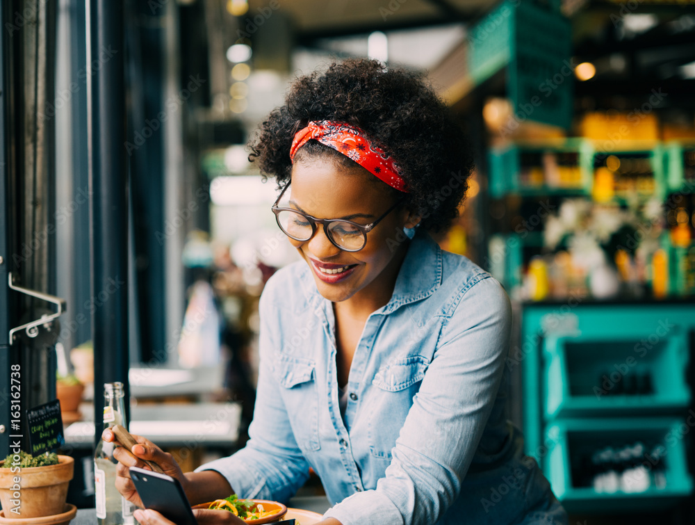 Smiling young woman reading a text message in a cafe