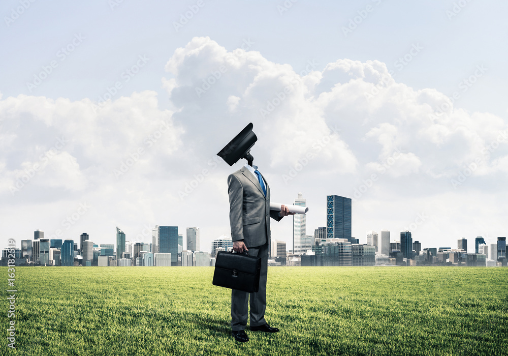 Camera headed man standing on green grass against modern citysca