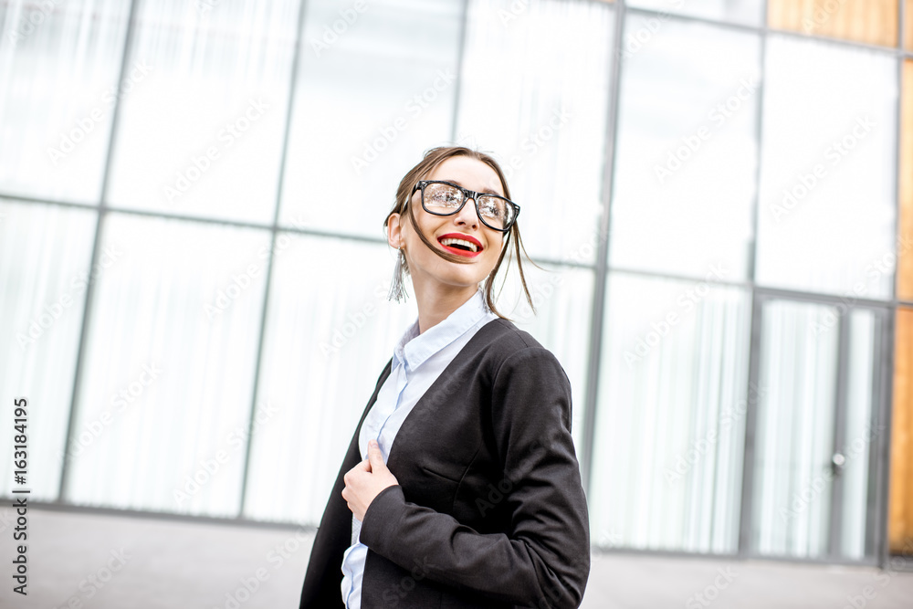 一位穿着西装的年轻女商人站在户外现代办公室墙上的肖像