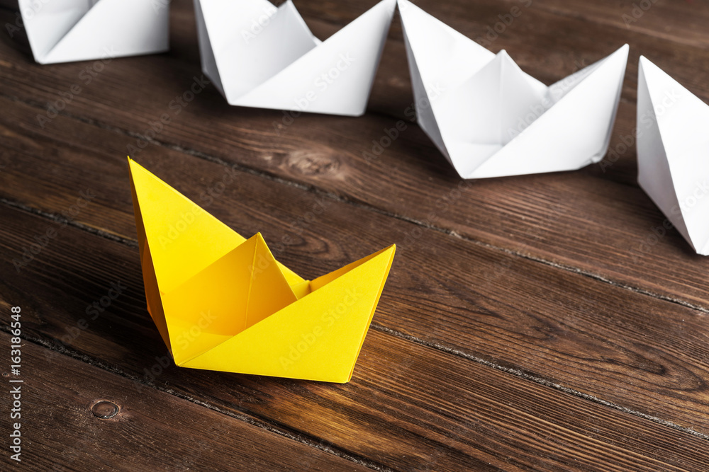 Business leadership concept with white and color paper boats on wooden table