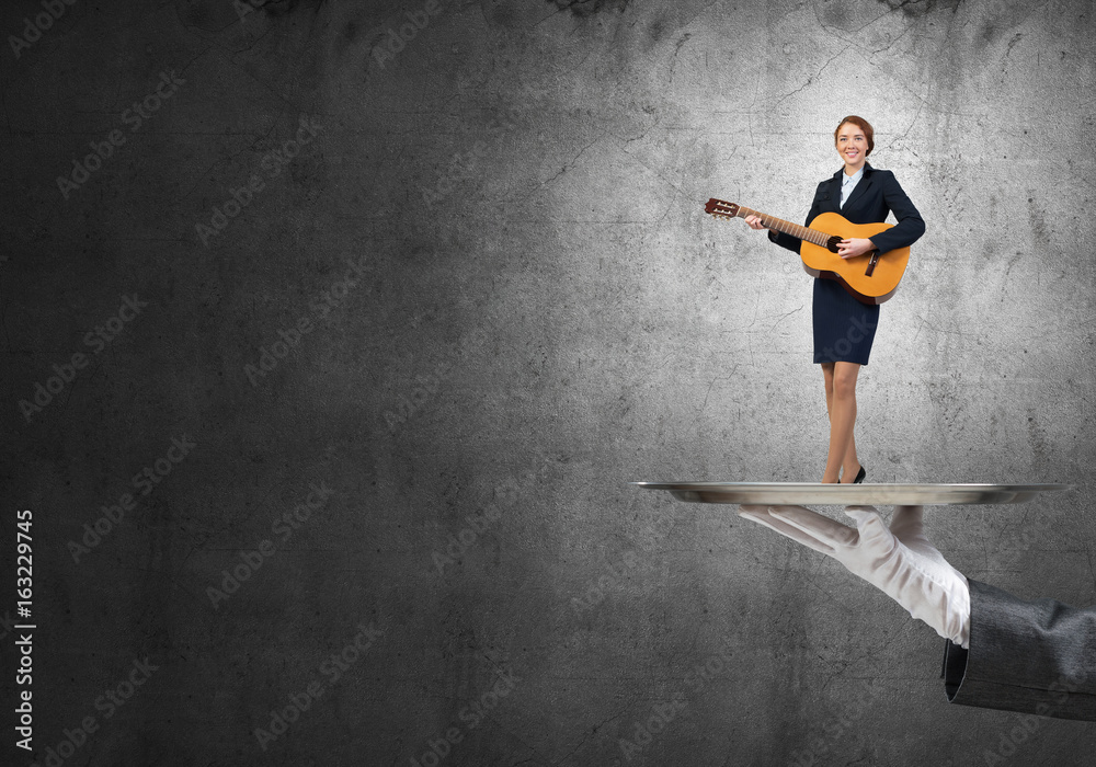 Attractive businesswoman on metal tray playing acoustic guitar against concrete wall background