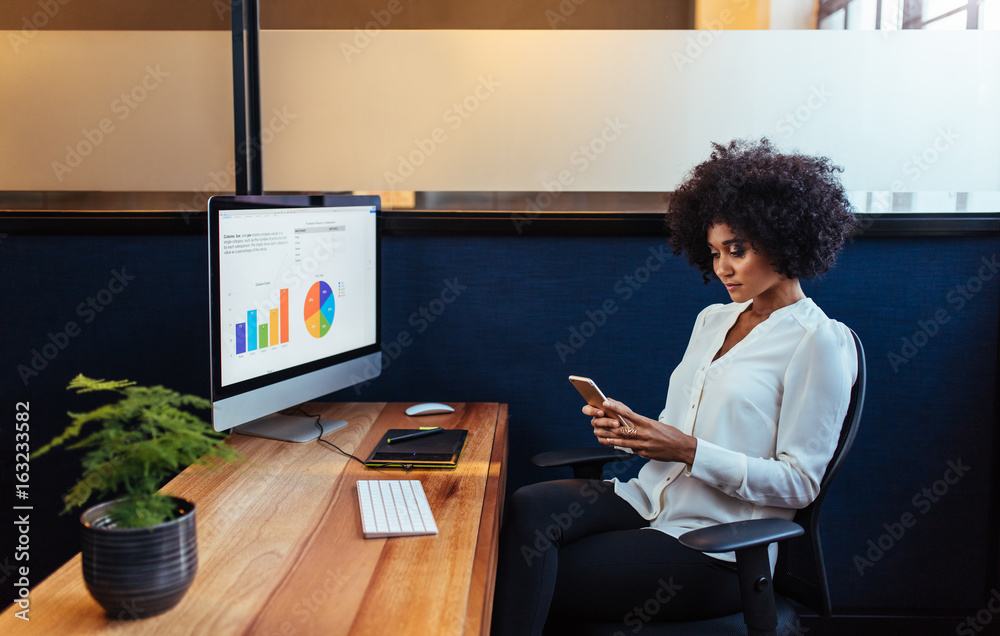 African businesswoman sitting at her desk using mobile phone