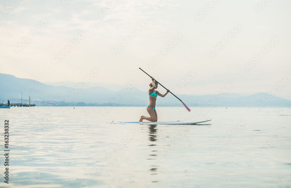 Young beautiful slavian woman tourist practicing paddle boarding in sea at beach near ancient fortre