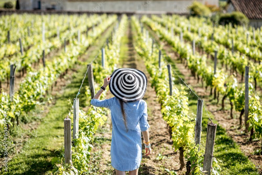 Young woman in striped hat enjoying beautiful sunset view on the vineyard in Bordeaux region in Fran