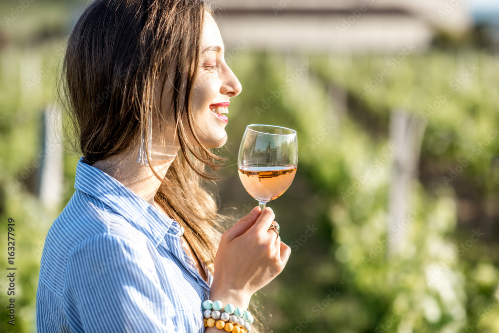 Young woman tasting wine standing outdoors on the vineyard in Bordeaux region during the sunset in F