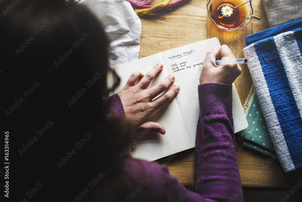 Aerial view of woman writing thread color list on notebook