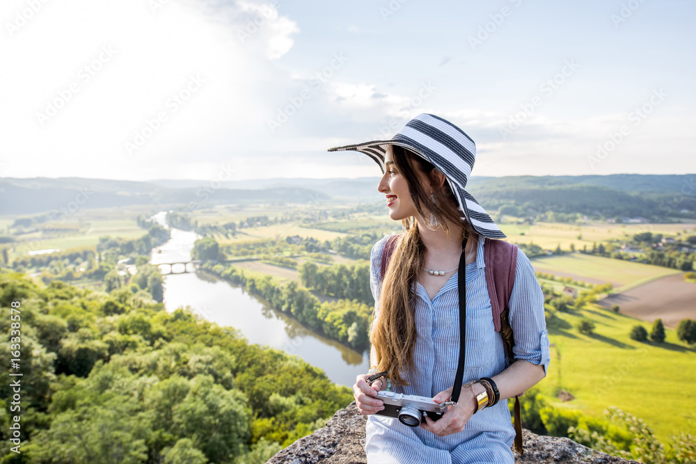 Young woman tourist in hat enjoying sunset view on the beautiful landscape with Dordogne river in Fr