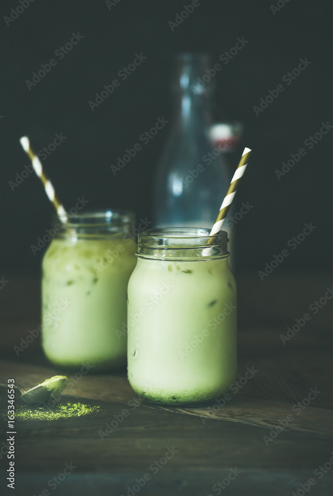 Cold refreshing iced coconut matcha latte drink in glass jars. Selective focus, copy space, dark tab