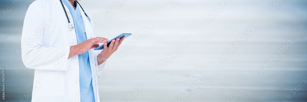 Doctor mid section holding tablet against blurry blue wood panel