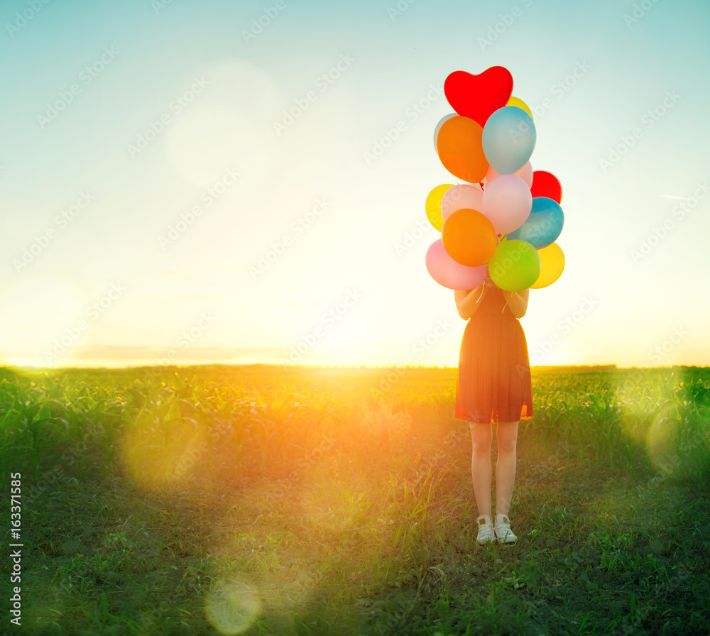 Beauty young woman on summer field with colorful air balloons over clear sky